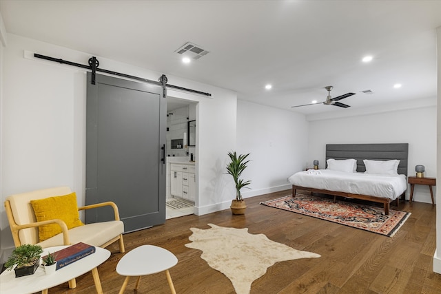 bedroom featuring ceiling fan, ensuite bathroom, dark wood-type flooring, and a barn door