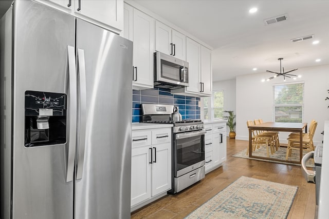 kitchen with white cabinets, tasteful backsplash, appliances with stainless steel finishes, a notable chandelier, and light wood-type flooring