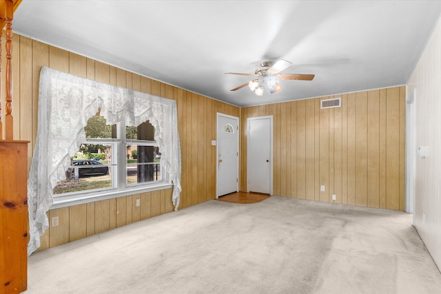 unfurnished room with wooden walls, ceiling fan, and light colored carpet