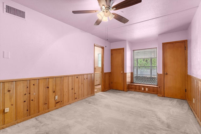 unfurnished room with wooden walls, ceiling fan, and light colored carpet