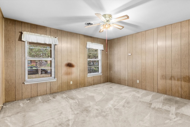 empty room with wood walls, ceiling fan, and light colored carpet