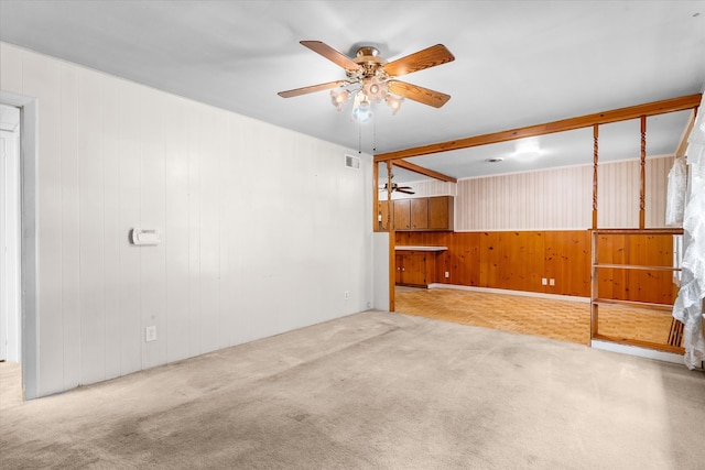 carpeted empty room featuring beamed ceiling, wood walls, and ceiling fan