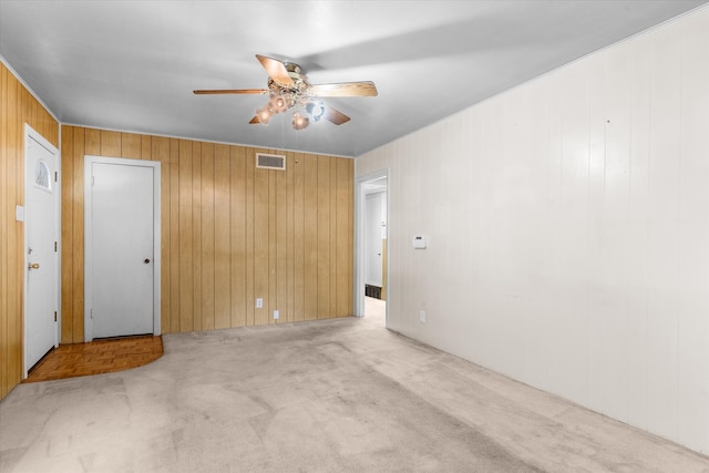 carpeted spare room featuring wooden walls and ceiling fan