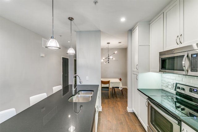 kitchen featuring white cabinets, sink, decorative light fixtures, dark wood-type flooring, and stainless steel appliances