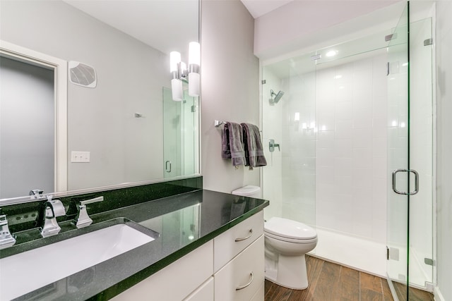 bathroom with wood-type flooring, vanity, a shower with shower door, and toilet