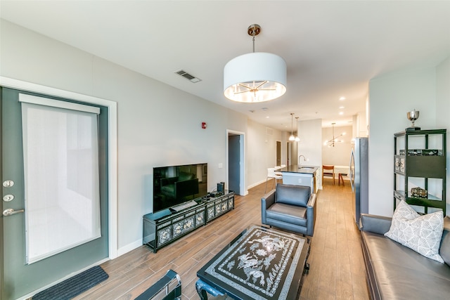 living room with light hardwood / wood-style floors, an inviting chandelier, and sink