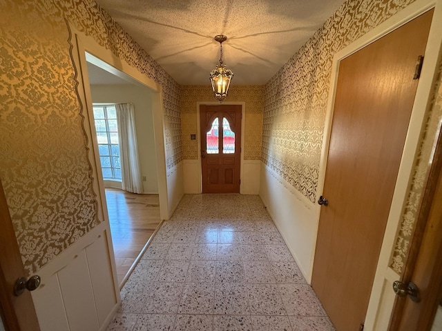 doorway to outside featuring plenty of natural light, a textured ceiling, and an inviting chandelier