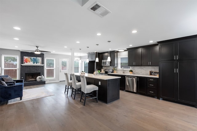 kitchen with a kitchen island, a healthy amount of sunlight, decorative light fixtures, and appliances with stainless steel finishes