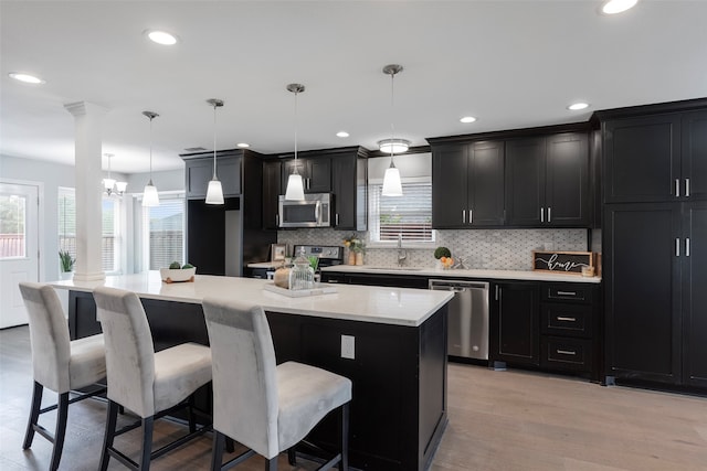 kitchen featuring a kitchen island, appliances with stainless steel finishes, a kitchen bar, hanging light fixtures, and light hardwood / wood-style floors