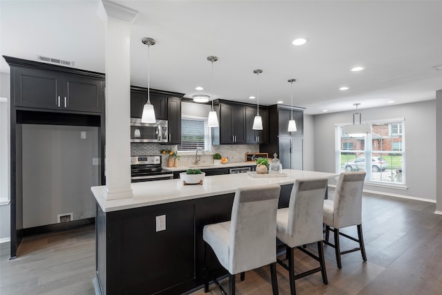 kitchen featuring hardwood / wood-style flooring, appliances with stainless steel finishes, a breakfast bar area, a center island, and pendant lighting