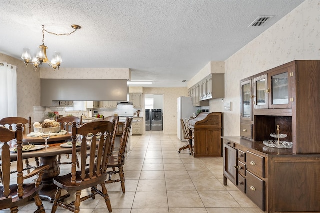 tiled dining space with a textured ceiling, washer and clothes dryer, and a chandelier