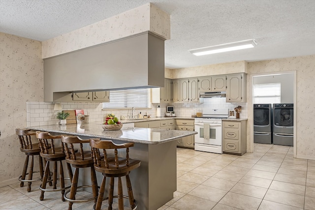 kitchen featuring separate washer and dryer, kitchen peninsula, a breakfast bar area, range hood, and white gas range