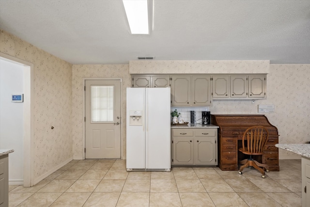 kitchen with light stone countertops, a textured ceiling, white refrigerator with ice dispenser, and light tile patterned floors