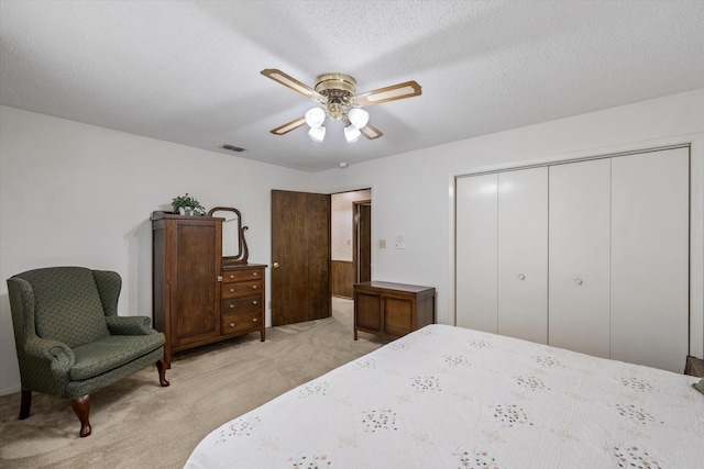 bedroom featuring a textured ceiling, light carpet, ceiling fan, and a closet