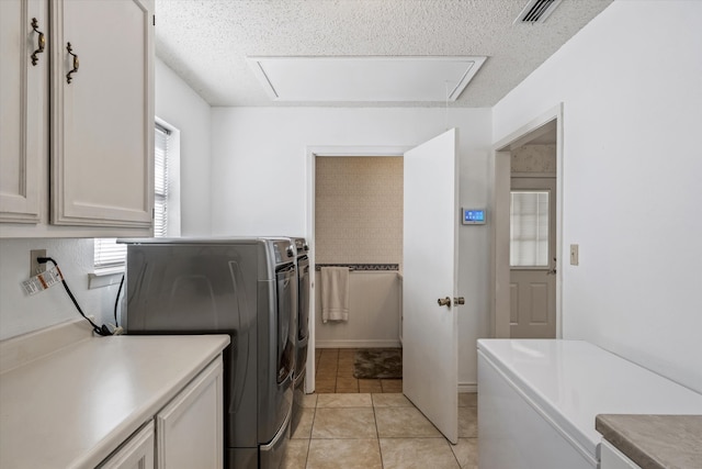 clothes washing area featuring cabinets, a textured ceiling, light tile patterned floors, and washing machine and clothes dryer