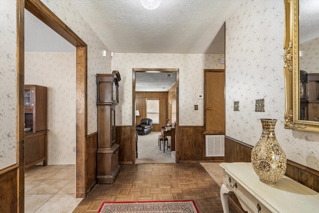 corridor with parquet flooring, wooden walls, and a textured ceiling