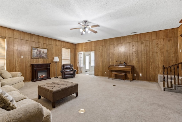 carpeted living room with ceiling fan, a textured ceiling, and wood walls