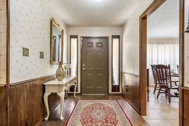 tiled entryway with wooden walls and a textured ceiling