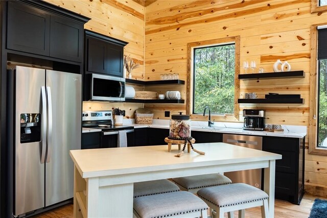 kitchen with dark cabinetry, open shelves, wooden walls, and appliances with stainless steel finishes