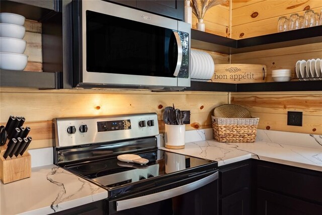 kitchen with decorative backsplash, dark cabinetry, light stone counters, and appliances with stainless steel finishes