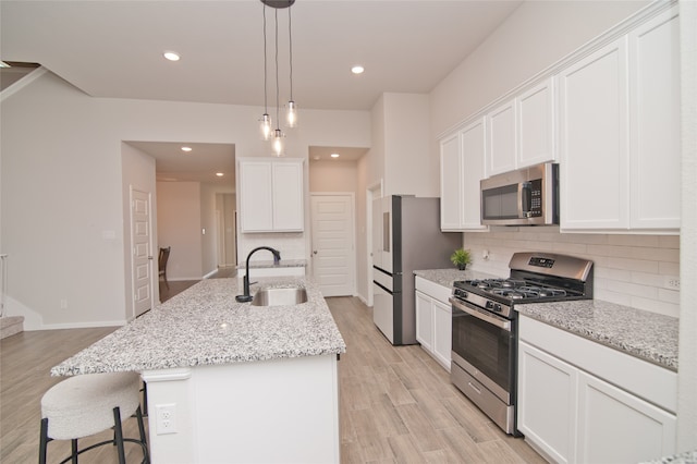 kitchen with sink, a kitchen island with sink, white cabinetry, stainless steel appliances, and light hardwood / wood-style floors