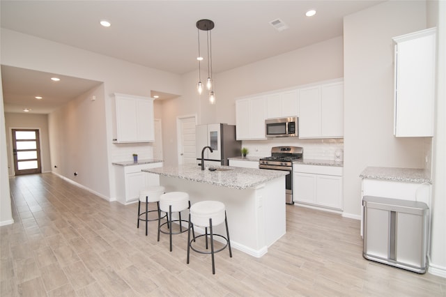 kitchen with appliances with stainless steel finishes, light stone counters, white cabinets, a kitchen island with sink, and sink