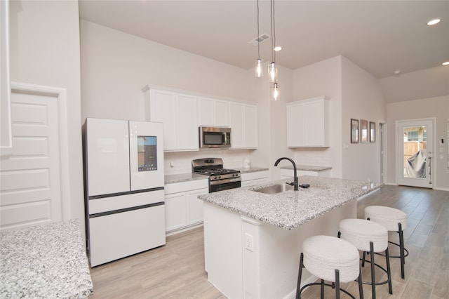 kitchen featuring light stone counters, light hardwood / wood-style floors, sink, stainless steel appliances, and a center island with sink