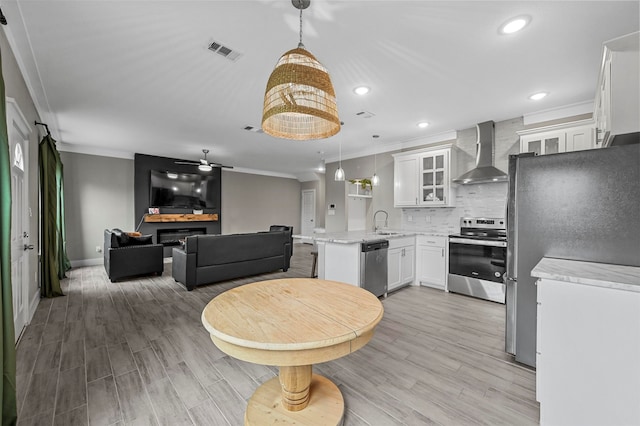 kitchen featuring kitchen peninsula, pendant lighting, wall chimney exhaust hood, and stainless steel appliances