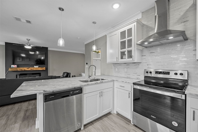 kitchen featuring sink, wall chimney exhaust hood, stainless steel appliances, kitchen peninsula, and white cabinets