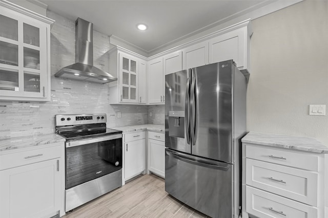 kitchen with light stone countertops, stainless steel appliances, white cabinetry, and wall chimney range hood