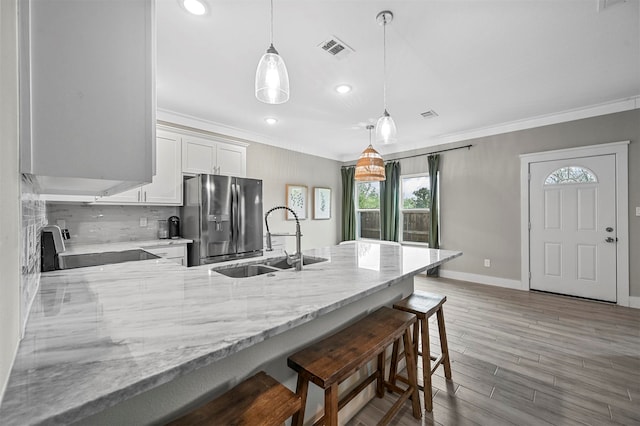 kitchen with stainless steel fridge, a kitchen breakfast bar, sink, white cabinetry, and hanging light fixtures