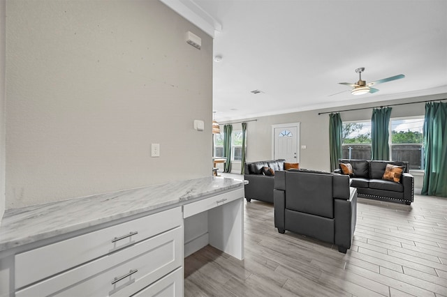 living room featuring built in desk, ceiling fan, and ornamental molding