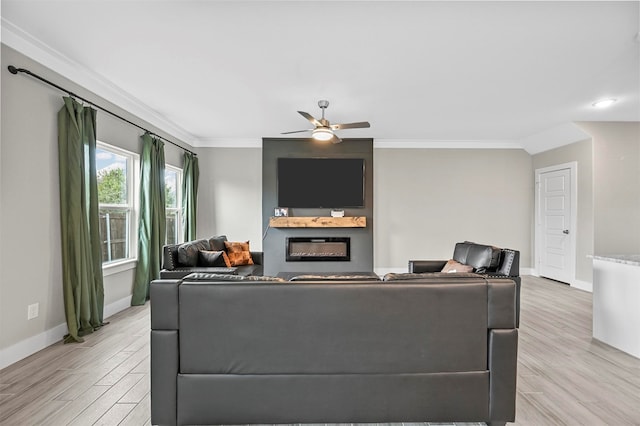 living room featuring ceiling fan, a large fireplace, ornamental molding, and light wood-type flooring