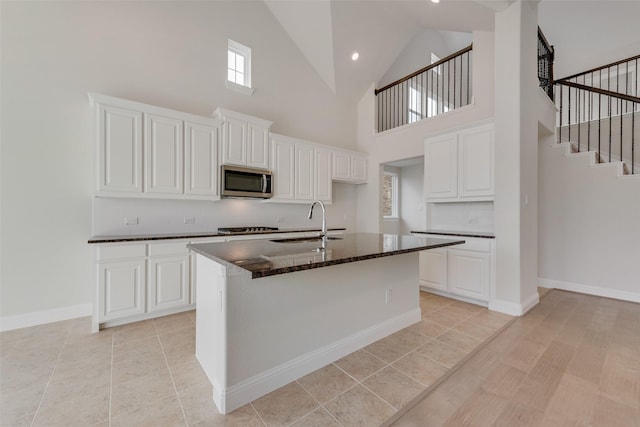 kitchen with a towering ceiling, white cabinetry, sink, backsplash, and a kitchen island with sink