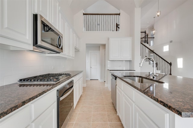 kitchen featuring sink, light tile patterned floors, appliances with stainless steel finishes, dark stone countertops, and white cabinets