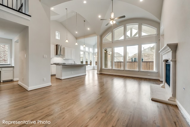 unfurnished living room with a high ceiling, light hardwood / wood-style flooring, and ceiling fan