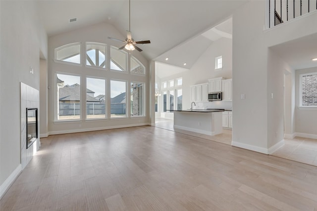 unfurnished living room with ceiling fan, sink, light hardwood / wood-style flooring, and a high ceiling