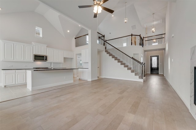 unfurnished living room with a tile fireplace, a towering ceiling, ceiling fan, and light hardwood / wood-style floors