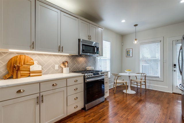 kitchen featuring dark hardwood / wood-style floors, tasteful backsplash, white cabinets, appliances with stainless steel finishes, and decorative light fixtures