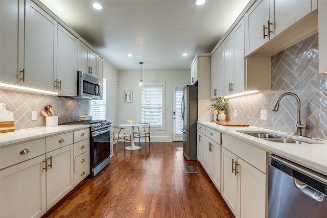 kitchen with appliances with stainless steel finishes, hanging light fixtures, backsplash, dark hardwood / wood-style flooring, and sink