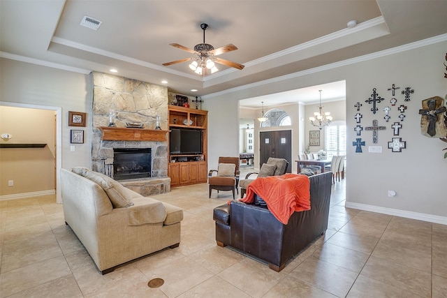 living room featuring a tray ceiling, ceiling fan with notable chandelier, light tile patterned floors, a stone fireplace, and ornamental molding