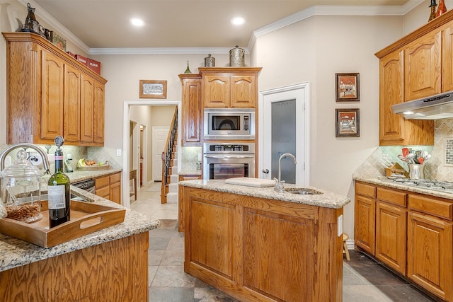 kitchen featuring an island with sink, sink, tasteful backsplash, exhaust hood, and appliances with stainless steel finishes