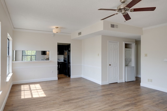 unfurnished living room with stacked washer and clothes dryer, light wood-type flooring, ornamental molding, and a textured ceiling