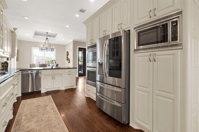 kitchen with appliances with stainless steel finishes, hanging light fixtures, kitchen peninsula, dark hardwood / wood-style flooring, and an inviting chandelier