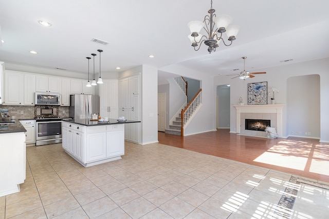 kitchen with a tile fireplace, white cabinetry, pendant lighting, and appliances with stainless steel finishes