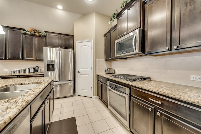 kitchen featuring decorative backsplash, light tile patterned floors, light stone counters, dark brown cabinetry, and stainless steel appliances