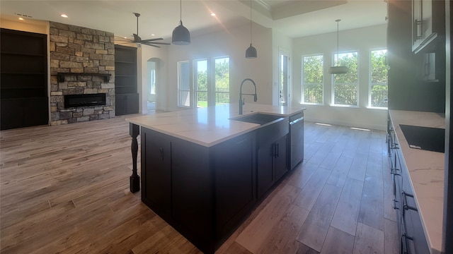 kitchen featuring an island with sink, sink, light hardwood / wood-style floors, decorative light fixtures, and black electric stovetop