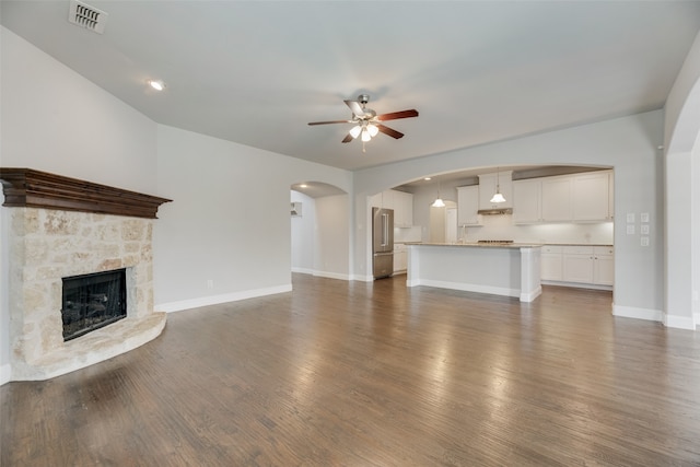 unfurnished living room with ceiling fan, a stone fireplace, and dark hardwood / wood-style floors