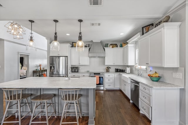 kitchen featuring stainless steel appliances, custom range hood, white cabinetry, and pendant lighting