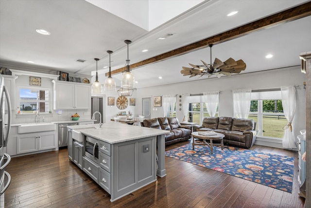 kitchen featuring a center island with sink, dark hardwood / wood-style floors, hanging light fixtures, sink, and beamed ceiling